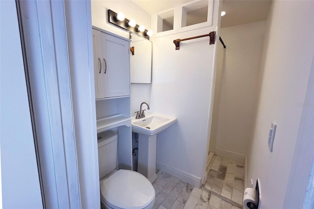 bathroom with toilet, marble finish floor, and baseboards