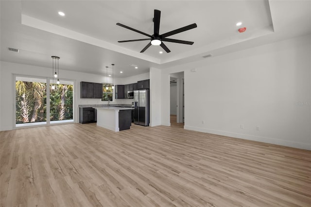 unfurnished living room with light wood-type flooring, a tray ceiling, visible vents, and baseboards