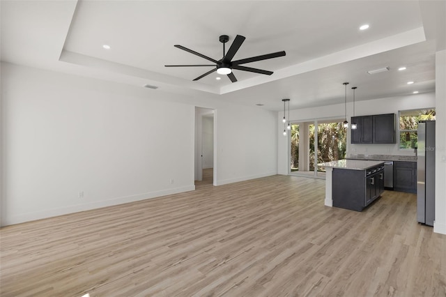 kitchen with stainless steel appliances, a tray ceiling, open floor plan, and light wood-type flooring