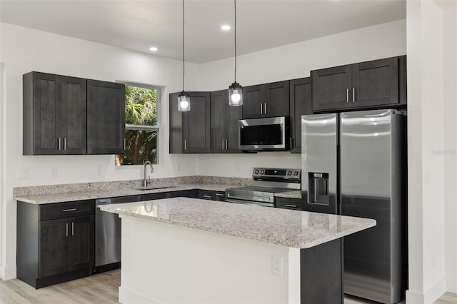 kitchen featuring a center island, stainless steel appliances, a sink, light stone countertops, and light wood-type flooring