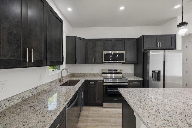 kitchen featuring light stone counters, light wood finished floors, recessed lighting, appliances with stainless steel finishes, and a sink