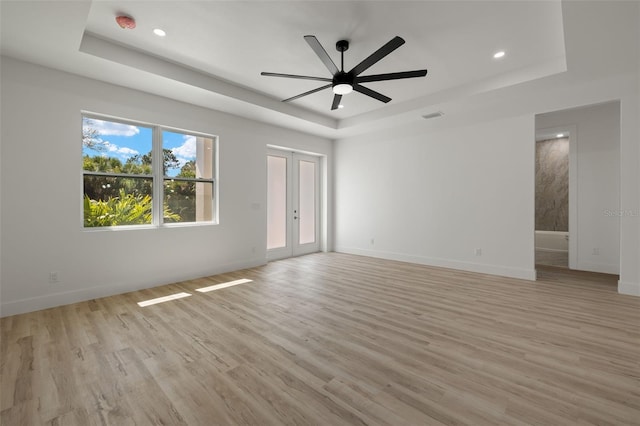 empty room with french doors, a raised ceiling, and light wood-style floors