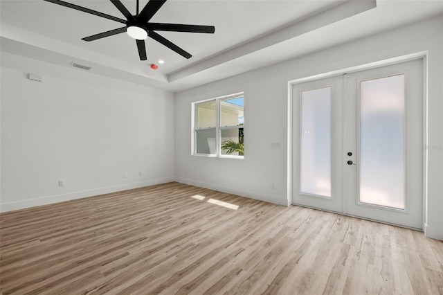 unfurnished room featuring visible vents, baseboards, a raised ceiling, light wood-style flooring, and french doors