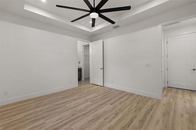 spare room featuring a raised ceiling, visible vents, baseboards, and light wood finished floors