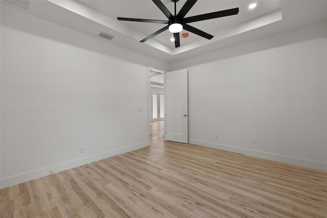 empty room with light wood finished floors, baseboards, visible vents, a raised ceiling, and a ceiling fan