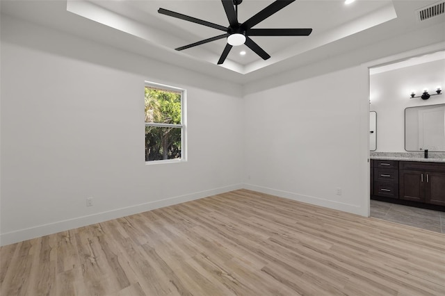 interior space with light wood-style floors, a raised ceiling, visible vents, and baseboards