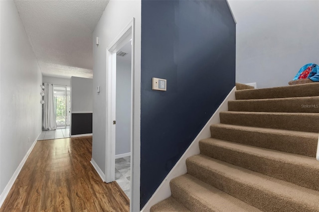 stairs with visible vents, baseboards, a textured ceiling, and wood finished floors