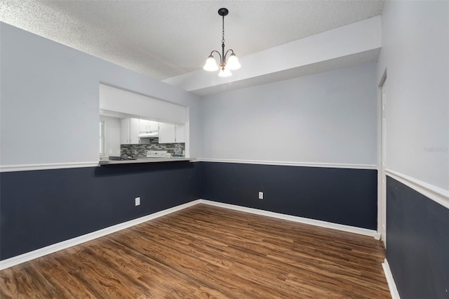 spare room featuring dark wood finished floors, a notable chandelier, a textured ceiling, and baseboards