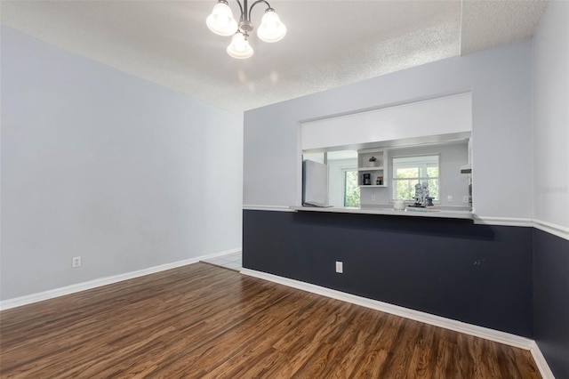 empty room featuring baseboards, wood finished floors, a textured ceiling, and a chandelier