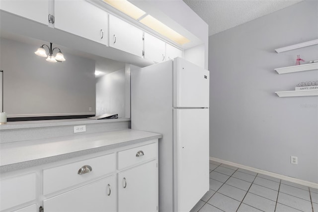 kitchen with light tile patterned flooring, freestanding refrigerator, light countertops, white cabinets, and a textured ceiling