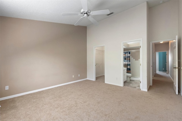 unfurnished bedroom with a walk in closet, light carpet, high vaulted ceiling, visible vents, and baseboards