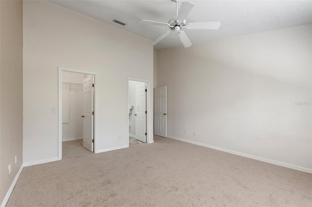 unfurnished bedroom featuring baseboards, visible vents, a spacious closet, a textured ceiling, and light carpet