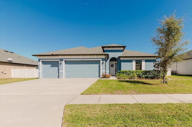 prairie-style house featuring a front yard, fence, stucco siding, concrete driveway, and a garage