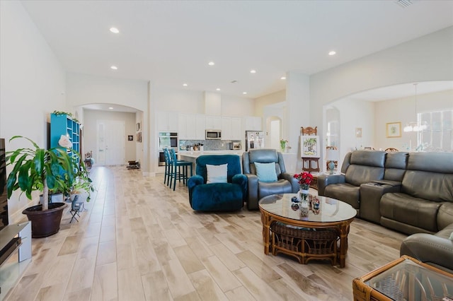 living room featuring a notable chandelier, recessed lighting, arched walkways, and light wood-type flooring