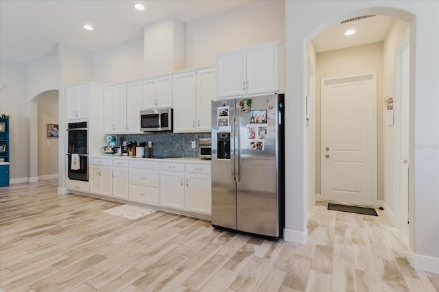 kitchen featuring arched walkways, tasteful backsplash, appliances with stainless steel finishes, and white cabinetry