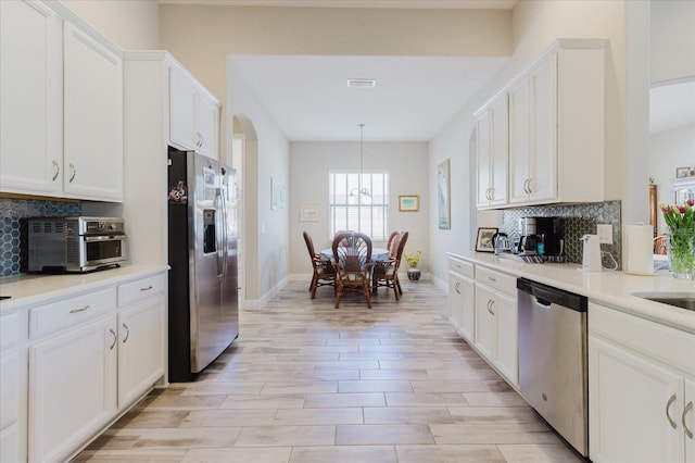 kitchen featuring visible vents, arched walkways, decorative backsplash, appliances with stainless steel finishes, and white cabinetry