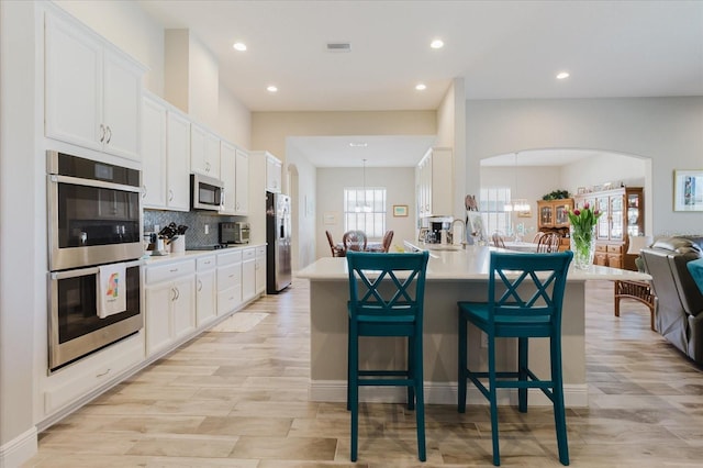 kitchen featuring open floor plan, white cabinets, appliances with stainless steel finishes, and a breakfast bar area