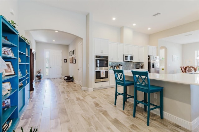 kitchen featuring arched walkways, backsplash, white cabinetry, and stainless steel appliances