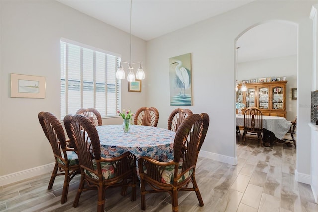 dining space featuring baseboards, arched walkways, light wood finished floors, and a chandelier