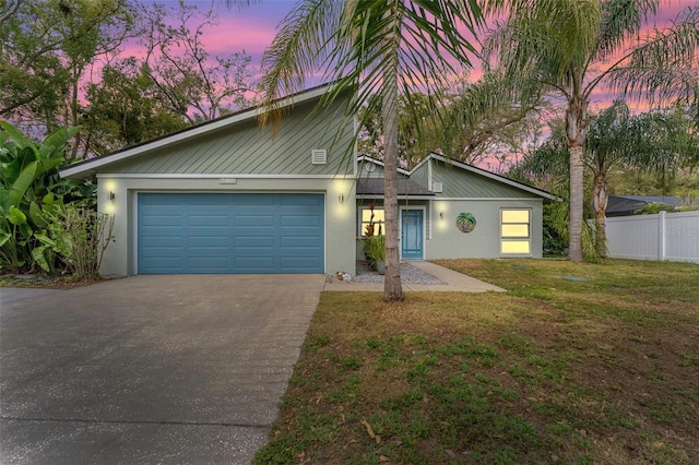 mid-century home featuring an attached garage, fence, a yard, driveway, and stucco siding