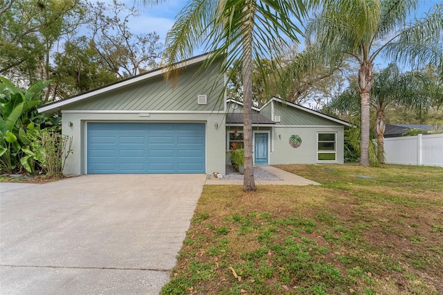 mid-century inspired home featuring stucco siding, fence, a garage, driveway, and a front lawn