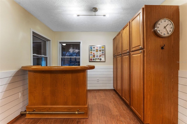 bar with wood finished floors, wainscoting, wooden walls, a textured ceiling, and a bar