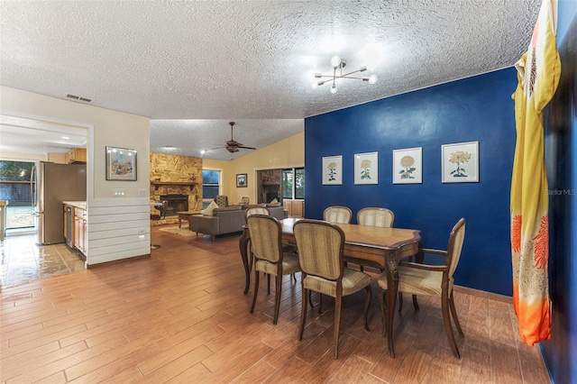 dining space featuring a fireplace, visible vents, a ceiling fan, vaulted ceiling, and light wood finished floors