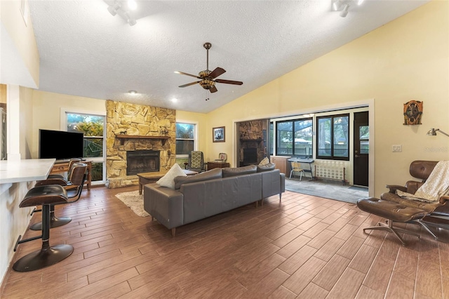 living area with a ceiling fan, wood finish floors, a fireplace, and a textured ceiling