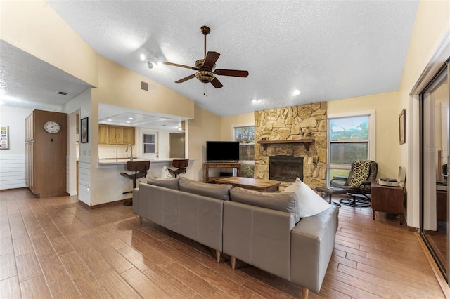 living area with lofted ceiling, a textured ceiling, a fireplace, and wood tiled floor