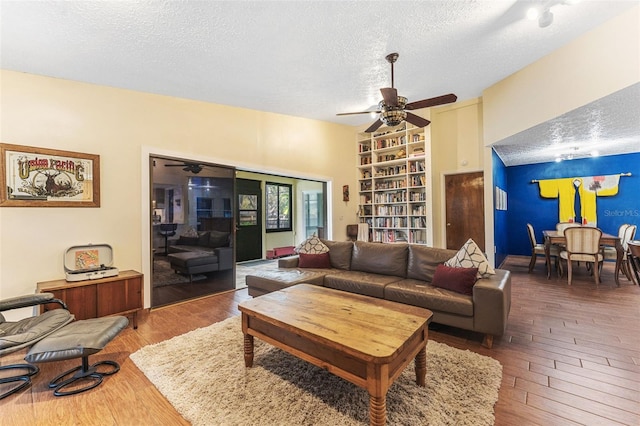 living area featuring a textured ceiling, built in shelves, hardwood / wood-style flooring, and a ceiling fan