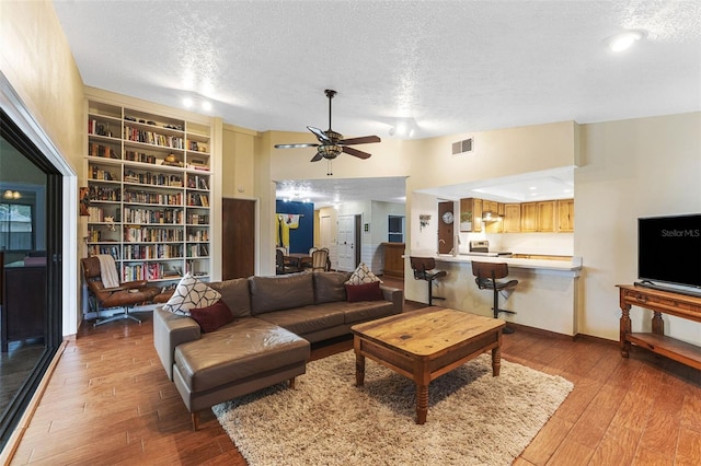 living area featuring a textured ceiling, a ceiling fan, visible vents, baseboards, and hardwood / wood-style floors