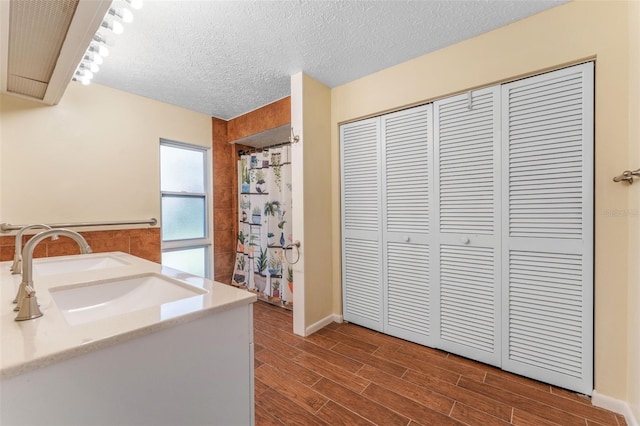 interior space featuring a shower with shower curtain, a textured ceiling, vanity, wood finish floors, and a closet