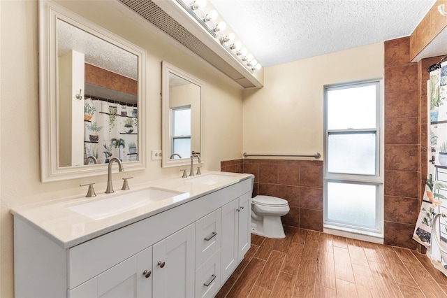 bathroom with a textured ceiling, a sink, and tile walls