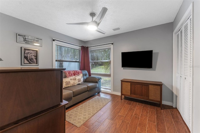 living area with ceiling fan, a textured ceiling, wood finished floors, visible vents, and baseboards