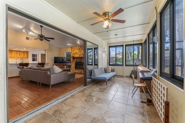 sunroom featuring a fireplace, visible vents, vaulted ceiling, a sink, and ceiling fan