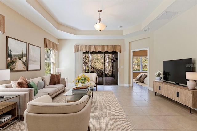 living room with light tile patterned floors, a raised ceiling, visible vents, and baseboards