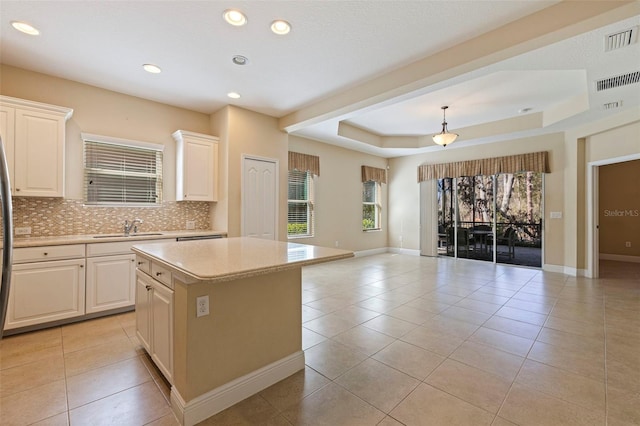 kitchen featuring light tile patterned floors, a sink, light countertops, a tray ceiling, and tasteful backsplash