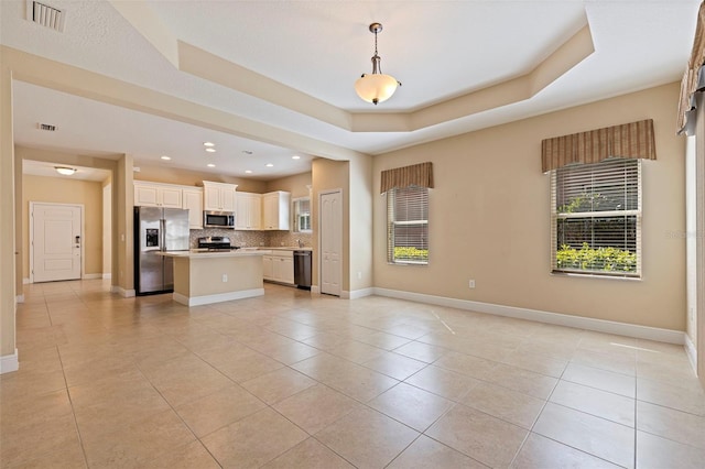 kitchen with stainless steel appliances, a kitchen island, visible vents, open floor plan, and a tray ceiling