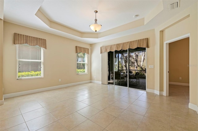 unfurnished room featuring light tile patterned floors, a tray ceiling, visible vents, and baseboards