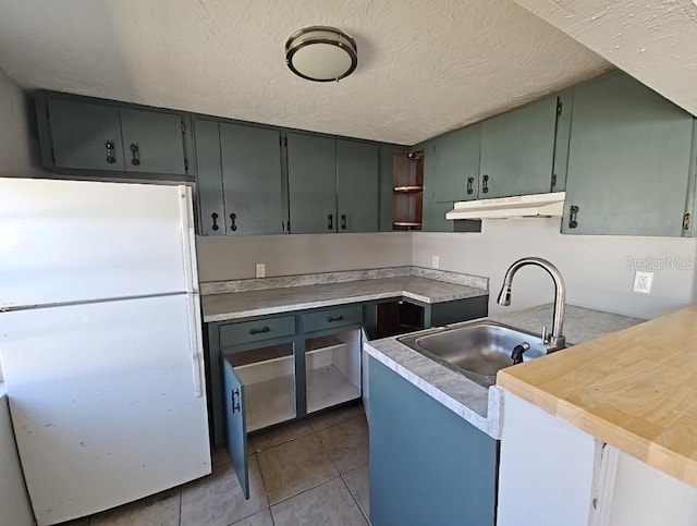 kitchen with dark tile patterned floors, freestanding refrigerator, a sink, a textured ceiling, and under cabinet range hood