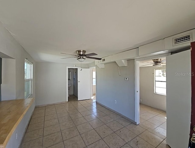 empty room with light tile patterned floors, a wealth of natural light, and a ceiling fan