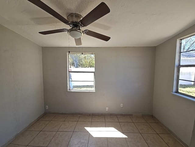 empty room with a textured ceiling, light tile patterned flooring, a wealth of natural light, and a ceiling fan