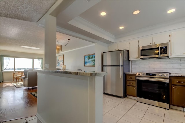 kitchen featuring light tile patterned floors, white cabinets, appliances with stainless steel finishes, ornamental molding, and backsplash