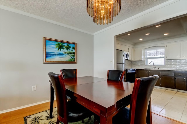 dining space featuring crown molding, an inviting chandelier, a textured ceiling, light wood-type flooring, and baseboards