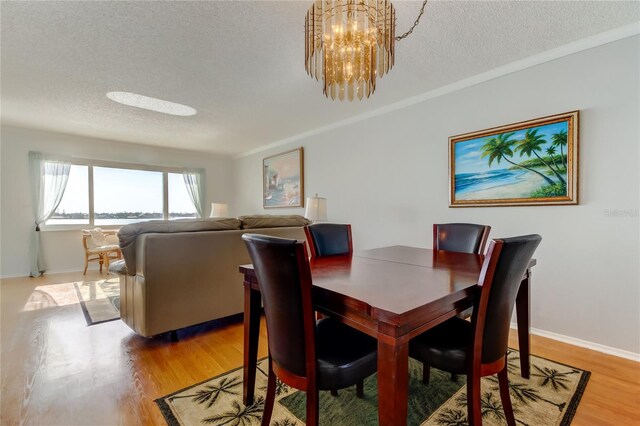 dining area with light wood-style floors, baseboards, a textured ceiling, and an inviting chandelier