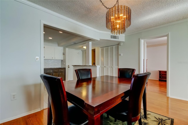 dining room with crown molding, light wood finished floors, visible vents, an inviting chandelier, and a textured ceiling