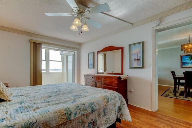 bedroom featuring a textured ceiling, ceiling fan with notable chandelier, baseboards, light wood-style floors, and ornamental molding