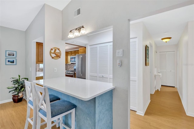 11430 94th St, Largo, FL 33773 - kitchen featuring a breakfast bar area, brown cabinets, stainless steel appliances, visible vents, and light wood-style floors