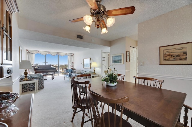 carpeted dining room featuring a ceiling fan, visible vents, and a textured ceiling