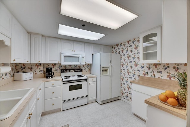 kitchen featuring white appliances, wallpapered walls, white cabinets, light countertops, and a sink